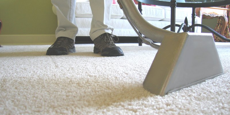 Person using a carpet cleaning machine on plush carpet in a living room setting, emphasizing professional cleaning services for residential interiors.