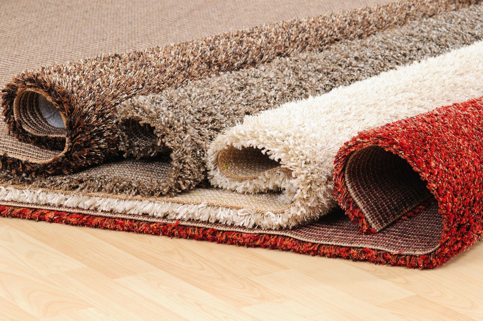 Rolled carpets in various textures and colors on a wooden floor, highlighting options for move-out carpet cleaning services.