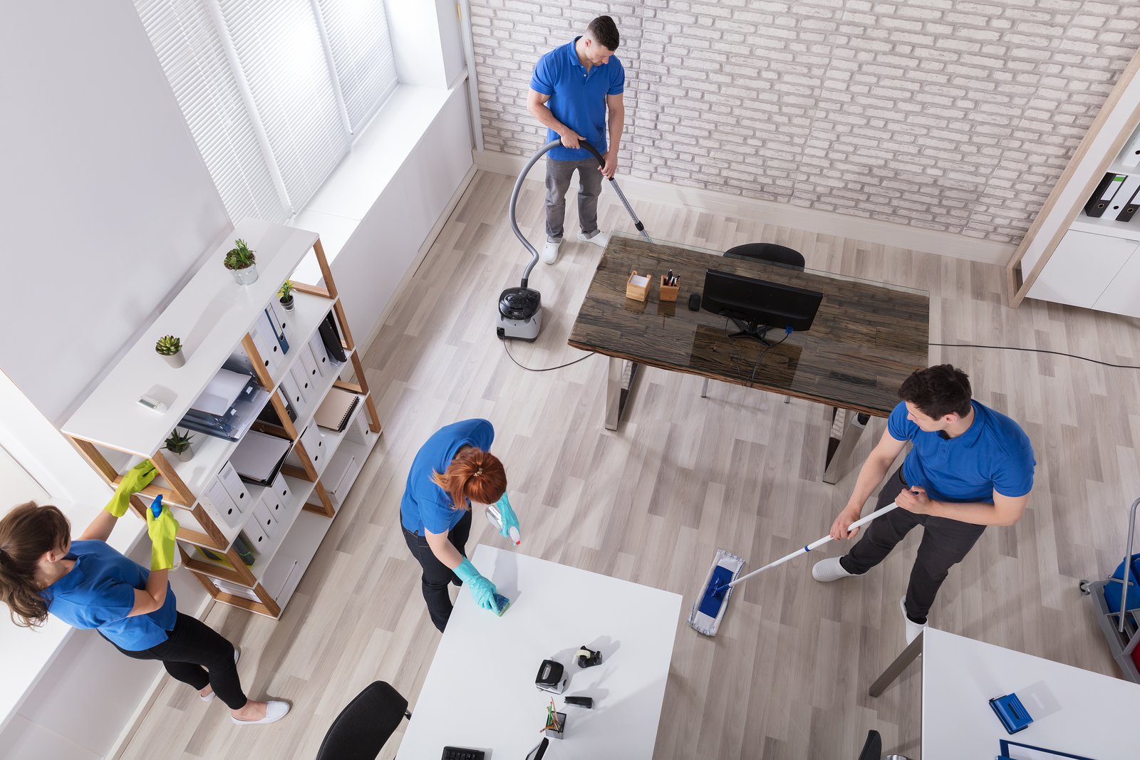 Team of professional cleaners in blue uniforms performing specialized cleaning in a modern office space, using various cleaning tools and equipment.